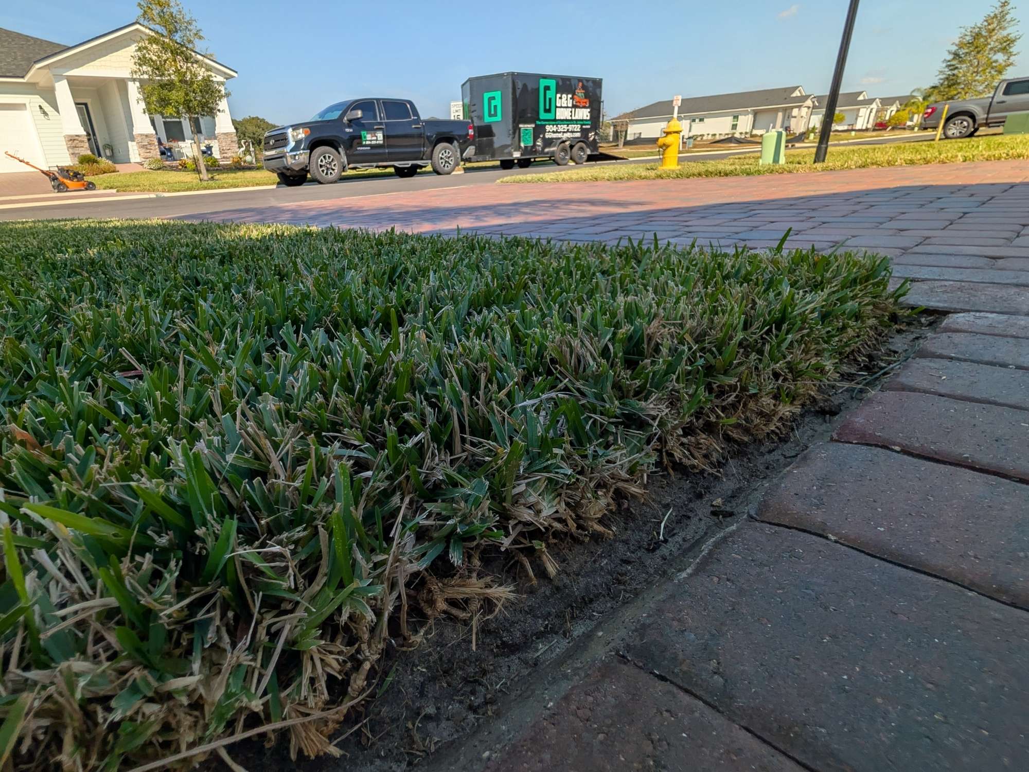 Crisp Lawn Edge Beside Brick Pavers - G&G Home Lawns Freshly edged lawn along brick pavers with G&G Home Lawns truck and trailer in the background
